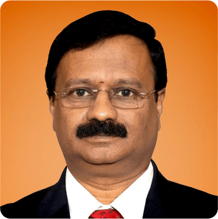 Portrait of Manivannan Subramanian wearing glasses, a dark suit, white shirt and red tie, photographed against a warm orange background.
